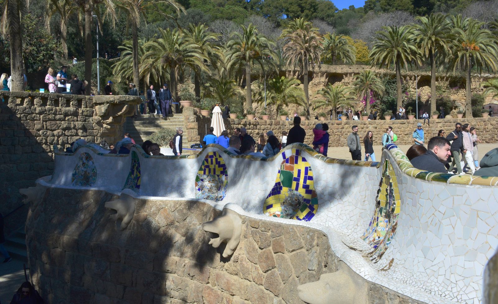Banco de trencadís na borda da praça principal do Park Güell, com a cidade ao fundo