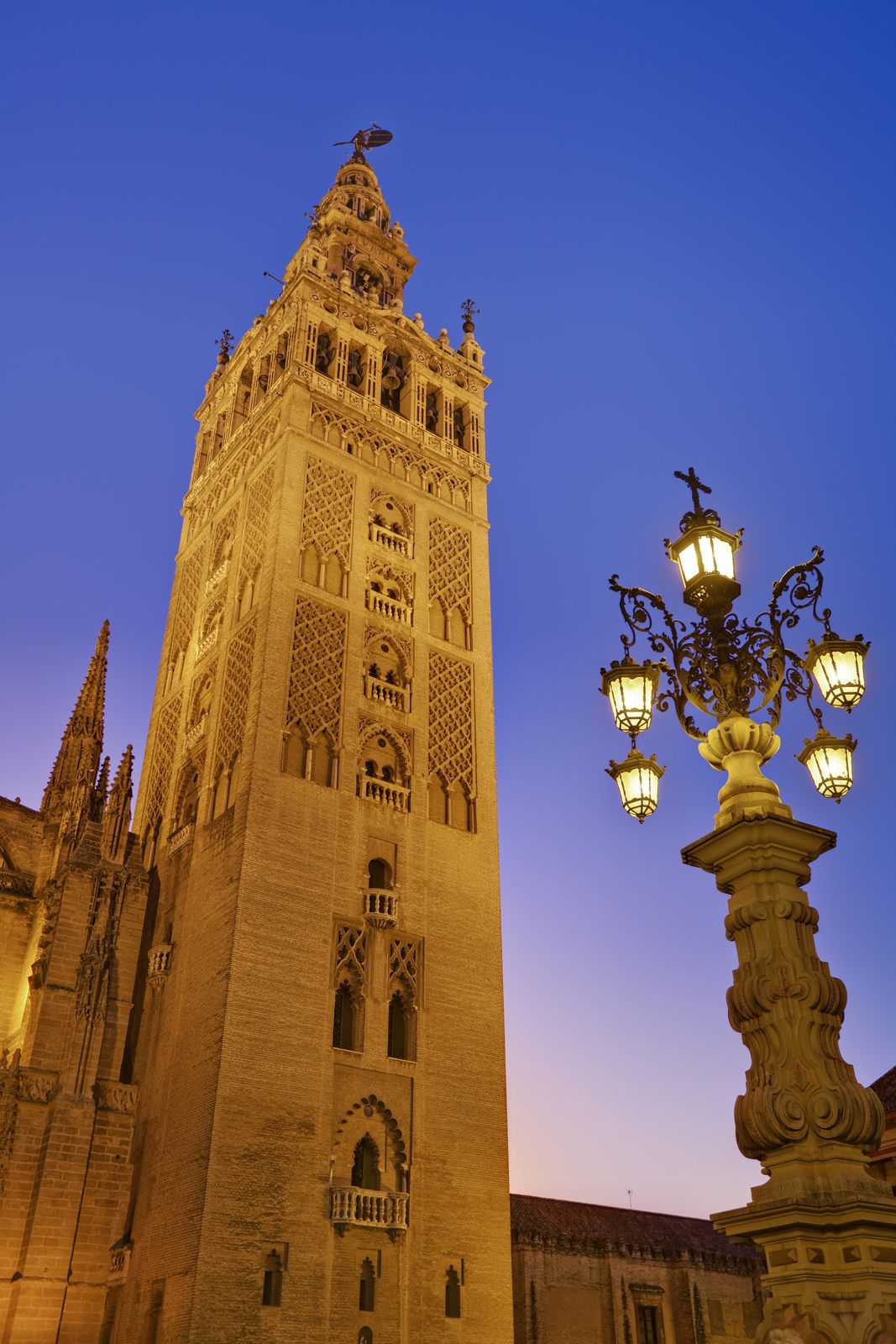 Giralda iluminada ao entardecer, com um poste de ferro em primeiro plano
